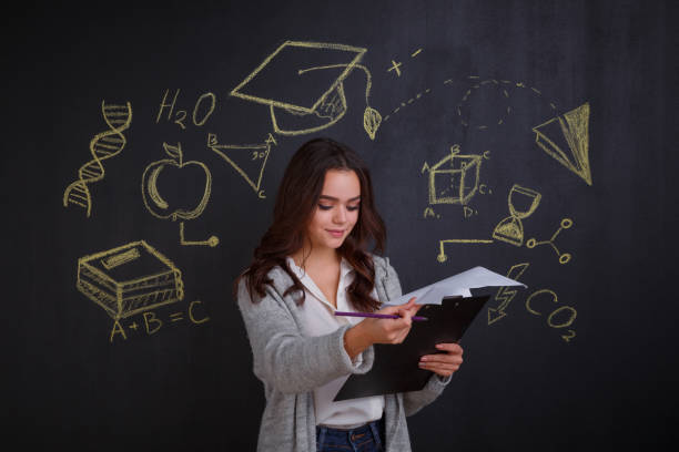 istock Young girl looking into a folder with papers, standing next to a whiteboard. 907567232