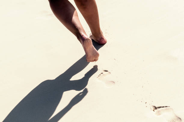 She’s a toes in the sand kinda girl Back view of African american woman walks on a sand beach. Close up of female feet and golden sand. Beach walk. Photo of Summer activity. Beautiful holiday background. Young girl walking alone on the sandy tropical beach at sunrise. walking beach women sadness stock pictures, royalty-free photos & images