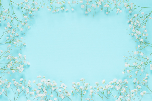 Floral greeting card for the spring holidays with copy space. Delicate small white flowers in a turquoise blue background, top view, mock up