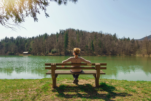 Young woman sitting on a bench near lake in spring time