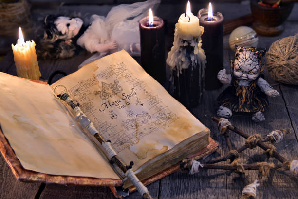 Old book with magic spells, scary doll, black candles and pentagram on witch table stock photo