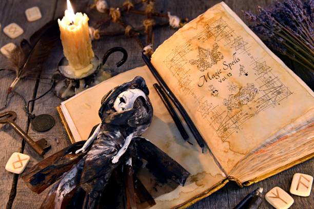 istock Old book with black magic spells, scary doll, rune and burning candle on planks 907610252