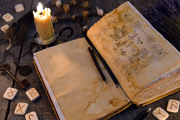 istock Open old book with magic spells, runes, candle and key on witch table 907610394