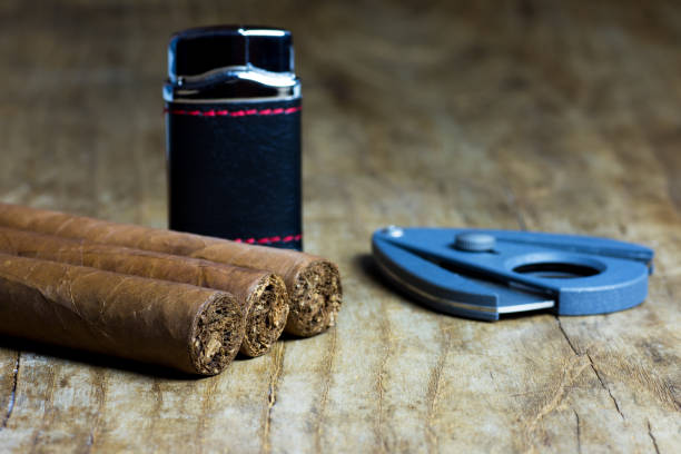 istock Three Cuban cigars with a lighter and a cutter on an old wooden board table 907611268