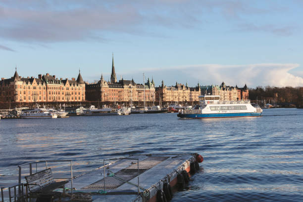 Stockholm, Sweden - December 10, 2017:  Pedestrians, ferries and cars on the Strandvagen waterfront reflecting the iconic facades of the Royal Dramatic Theatre, luxury hotels and townhouses that line the shore. Composite panoramic image created from eight contemporaneous sequential photographs.