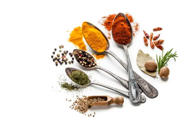 Top view of four old spoons with spices and herbs shot on white background. Spices and herb included are turmeric, bay leaf curry powder, nutmeg, peppercorns, paprika, mustard seeds and others. High key DSRL studio photo taken with Canon EOS 5D Mk II and Canon EF 100mm f/2.8L Macro IS USM