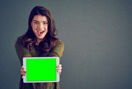 Studio shot of an cheerful young woman holding a digital tablet while standing against a dark background