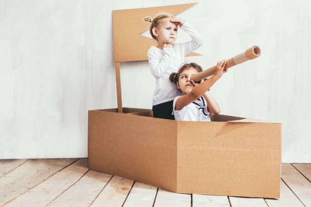 zwei kinder spielen kleine mädchen nach hause in einem karton schiff, kapitäne und matrosen - hoch position fotos stock-fotos und bilder