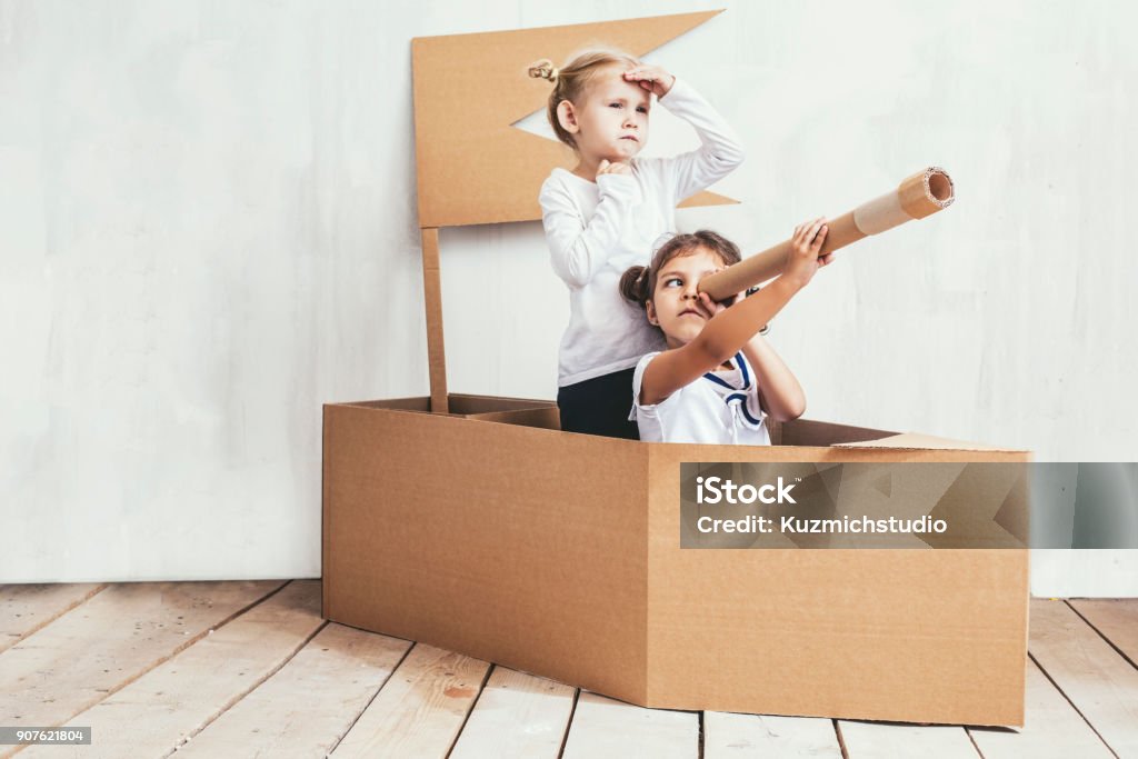 Due bambine bambini a casa in una nave di cartone giocano capitani e marinai - Foto stock royalty-free di Bambino