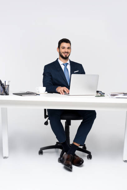 istock handsome young businessman smiling at camera while using laptop at workplace 907640380