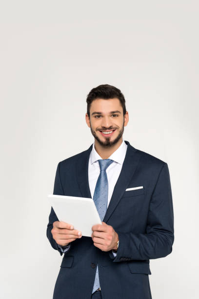 istock handsome young businessman holding digital tablet and smiling at camera isolated on grey 907646348