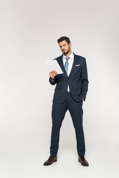 istock full length view of confident young businessman using digital tablet isolated on grey 907646412