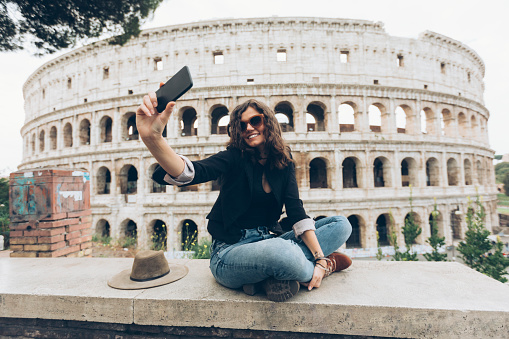 Young woman taking selfie on street in Italy, in front of Coliseum.