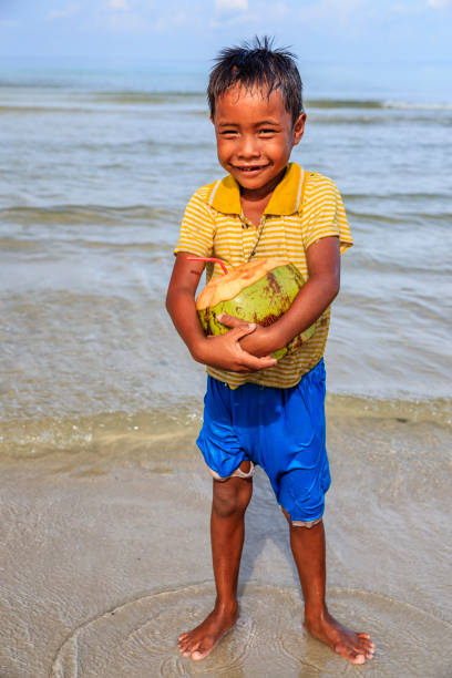 istock Cambodian little boy holding coconut on the beach, Cambodia 907663128