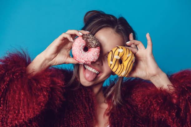 istock Attractive young woman in bright fur coat posing with donuts in hands. 907676358