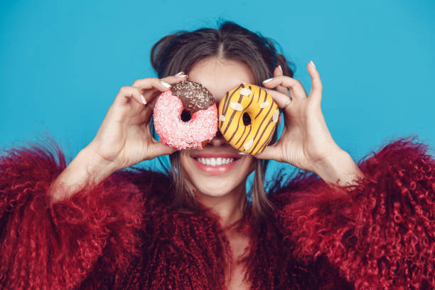 istock Attractive young woman in bright fur coat posing with donuts in hands. 907676396