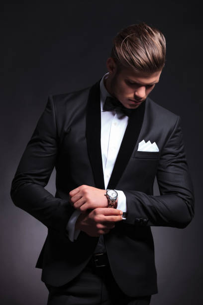 business man fixes and looks at cufflinks elegant young fashion man in tuxedo fixing his cufflinks while looking at them.on black background necktie businessman collar tied knot stock pictures, royalty-free photos & images