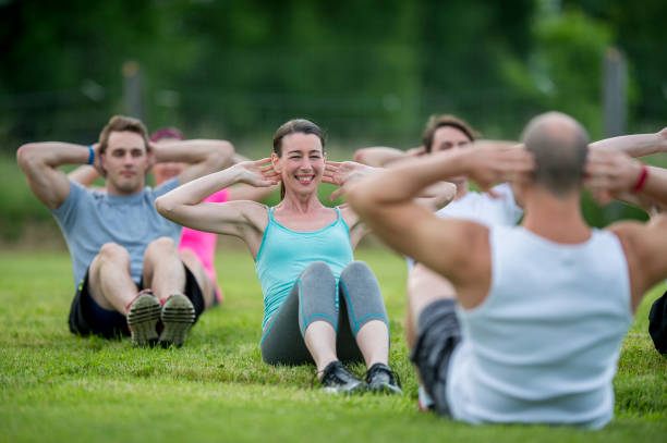 Boot Camp A group of adults are outdoors in a park. They are attending a fitness class lead by an instructor. They are sitting on the grass and doing sit-ups. fitness boot camp stock pictures, royalty-free photos & images