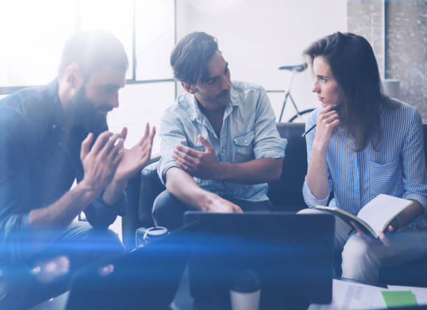 istock Coworking process in a sunny office.Young people making discussing at office.Business team sitting on the sofa and using mobile devices.Horizontal,blurred background, visual effects. 907686888