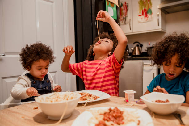 Children Eating Spaghetti and Yoghurt A family around a table eating spaghetti one child dangles spaghetti into his mouth spaghetti photos stock pictures, royalty-free photos & images