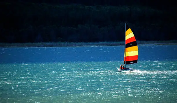 Colorful double hulled sailing boat sailing away with brightly colored sails