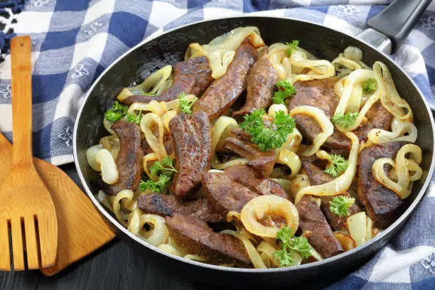 close-up of delicious veal liver pieces stir fried and stewed with onion rings in a skillet