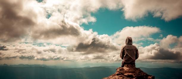 istock Lonely man sitting on top of mountain cloudy sky 907751720