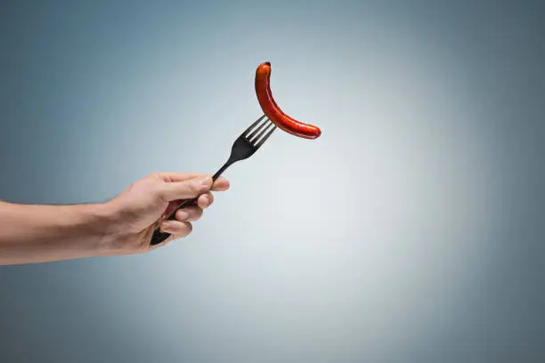 Photo of sausage on a fork in his hand
