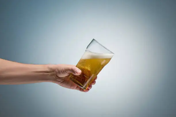 Closeup of a male hand holding up a glass of beer over a blue background