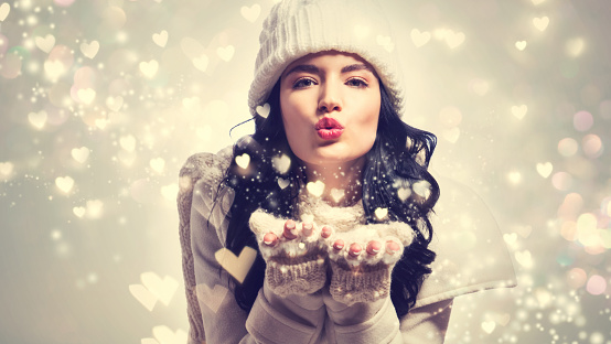 Happy young woman with winter clothes blowing snow and hearts