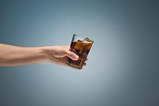 Drink cola in glass with hand on blue background.