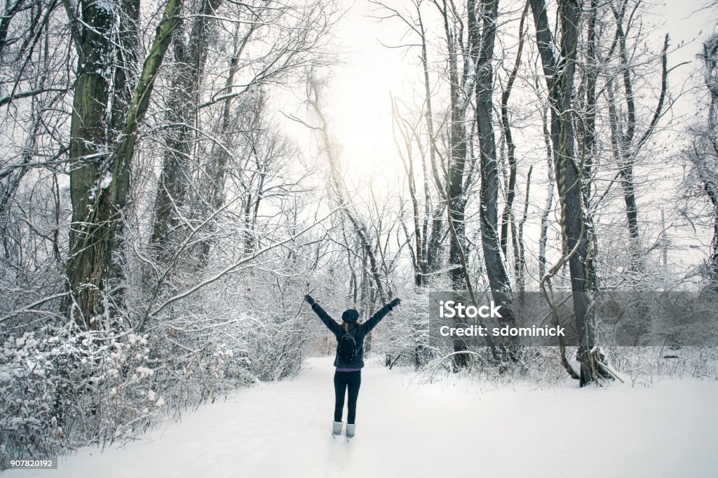 Woman Enjoying Snow Covered Forest A woman standing with her arms outstretched as she enjoys a walk in the forest on a beautiful winter day. Outdoors Stock Photo