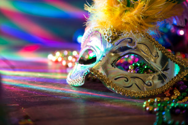 Mardi Gras, Rio carnival mask and colorful decorations. Mardi Gras or Rio Carnival mask and colorful carnival decorations. Scene includes: gold feathered mask, colored party lights, and beads. Objects lie on wooden table. No people. purple and gold masquerade masks stock pictures, royalty-free photos & images