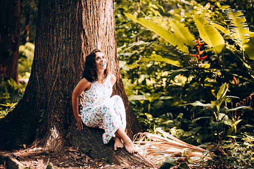 Happy young Brazilian woman sitting by the tree