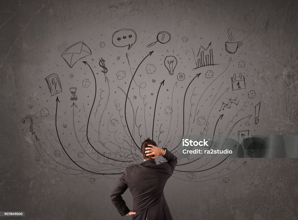 Businessman in front of a chalkboard deciding with arrows and signs Young businessman standing and deciding in front of a chalkboard with sketched arrows and signs in different directions Adult Stock Photo