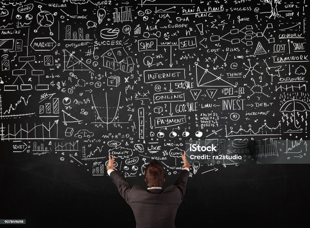 Businessman standing in front of drawn charts on a blackboard Young businessman standing in front of sketched charts and signs on a blackboard Data Stock Photo