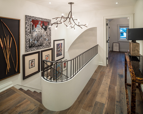 Toronto, Canada. Interior of modern hallway with grand stairs. Mix of design and style.  Variety of art on the wall. Open door of the top floor bedroom in the background.