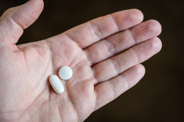 close-up view of a white male hand holding two white pills in the palm against a dark background - hydrocodone imagens e fotografias de stock