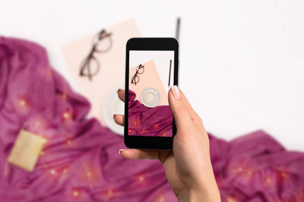 istock Female hand with a smartphone makes a photo workspace with notebook, coffee cup, scarf, glasses 907852470