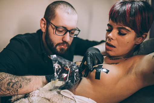 Man tattooing a woman in his tattoo studio.
