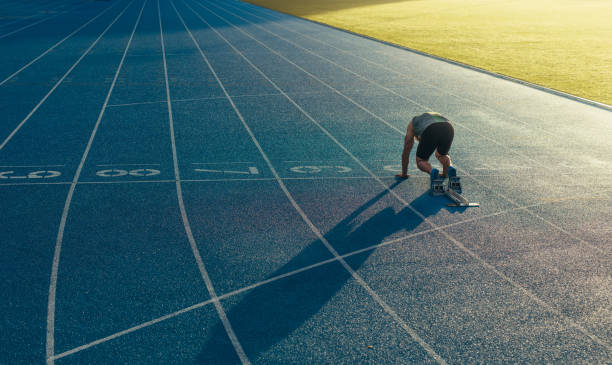 Sprinter on his marks on a running track Rear view of an athlete ready to sprint on an all-weather running track. Runner using a starting block to start his run on race track. scoring run stock pictures, royalty-free photos & images