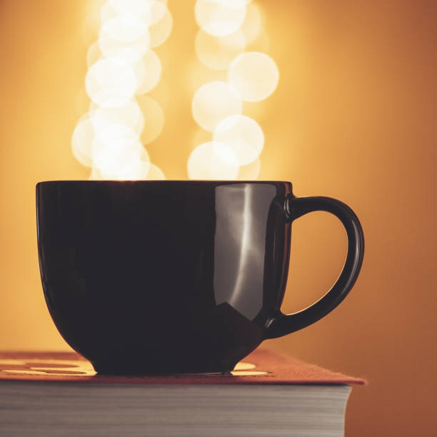 istock The black cup of tea on a book against blurred lights. 907856754