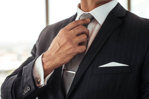 Cropped shot of businessman hand adjusting his necktie. Close up of man in business suit correcting tie.