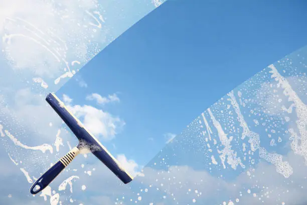 Photo of Rubber squeegee cleans a soaped window and clears a stripe of blue sky with clouds, concept for tranparency or spring cleaning, copy space in the background