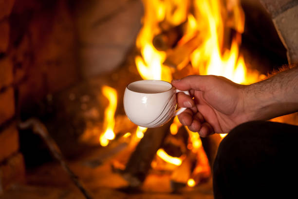 istock the man's hand with a cup by the fireplace 907860850