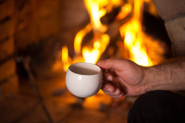 istock the man's hand with a cup by the fireplace 907860888