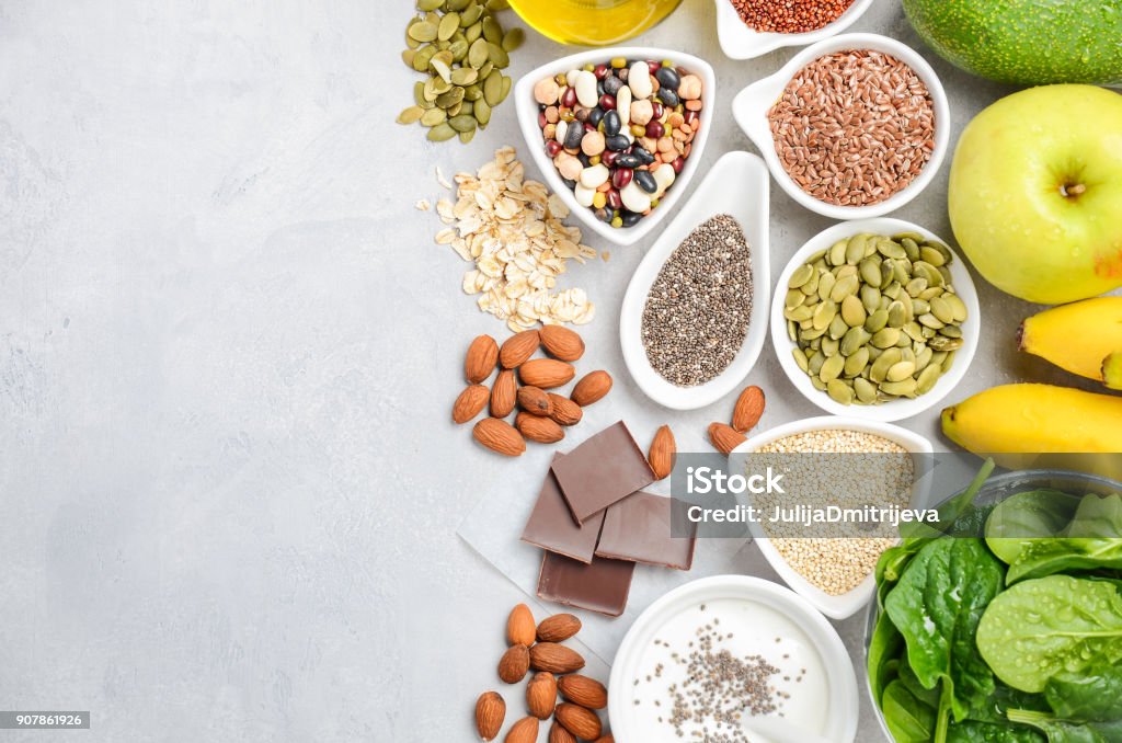 Healthy food nutrition dieting concept. Banana, chocolate, spinach, avocado, apple, quinoa, chia, flax seeds, yogurt, almond, beans, oat, pumpkin seeds, olive oil. Healthy food nutrition dieting concept. Banana, chocolate, spinach, avocado, apple, quinoa, chia, flax seeds, yogurt, almond, beans, oat, pumpkin seeds, olive oil. Top view, flat lay, copy space. Magnesium Stock Photo
