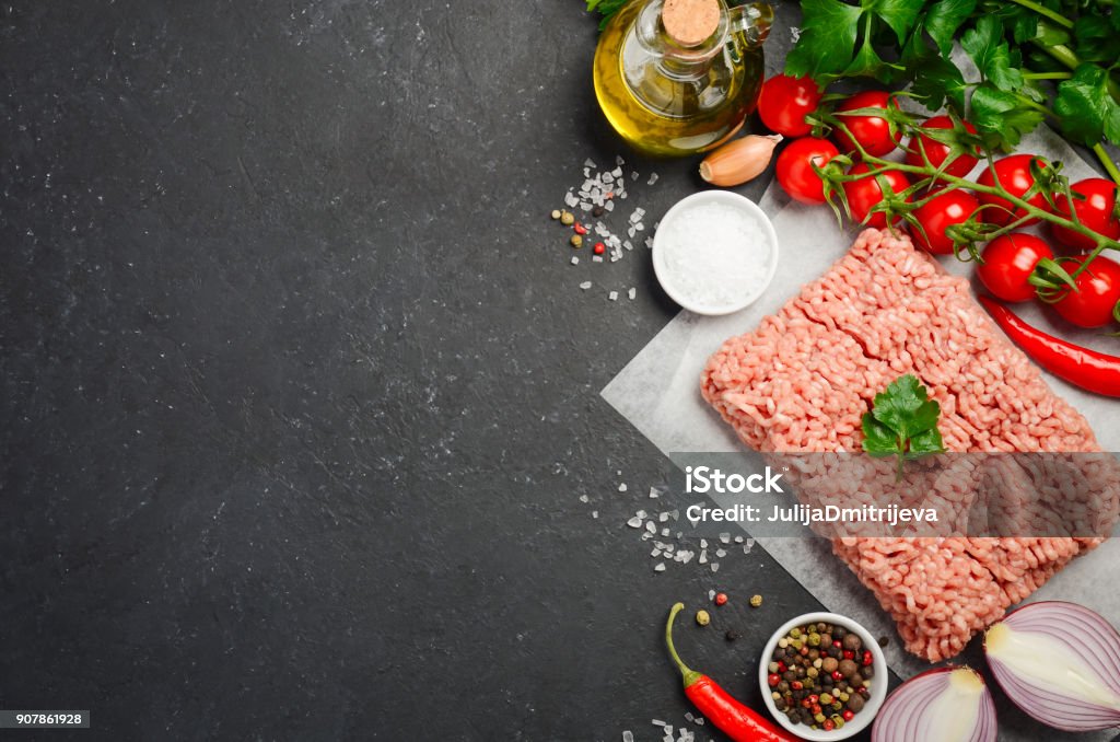 Raw minced meat on paper with fresh vegetables and spices on black background. Raw minced meat on paper with fresh vegetables and spices on black background top view copy space Backgrounds Stock Photo