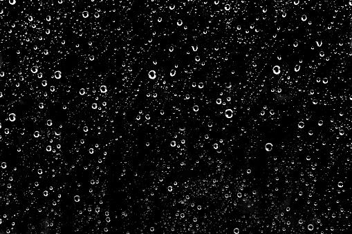 Hundreds of white rain drops on a glass window with a black background