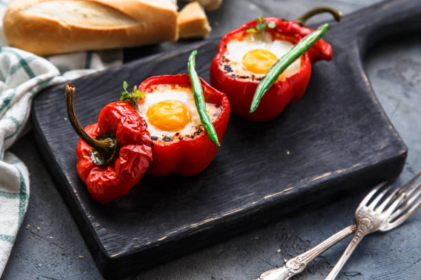 istock Egg baked in red bell pepper with sausage and tomato on a black board, close view 907867908